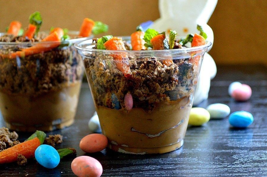 A cup of chocolate mousse topped with chocolate dirt and candied carrots