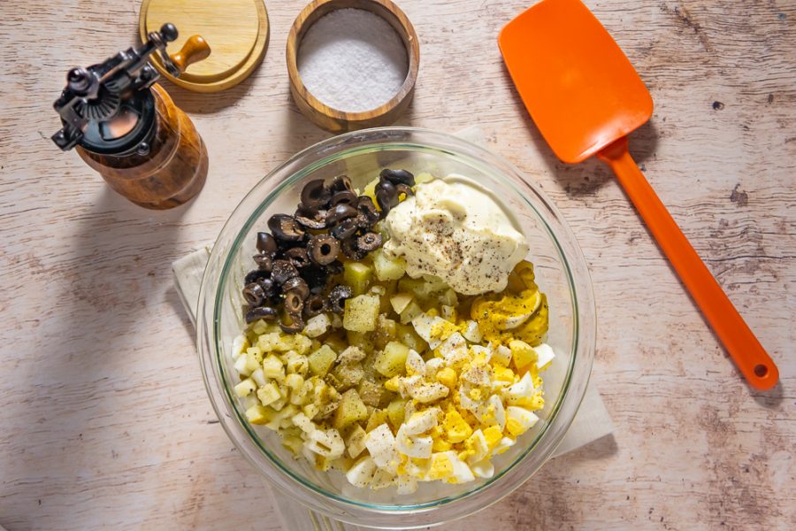 A bowl of potatoes with toppings like olives, eggs, pickles, and mayo