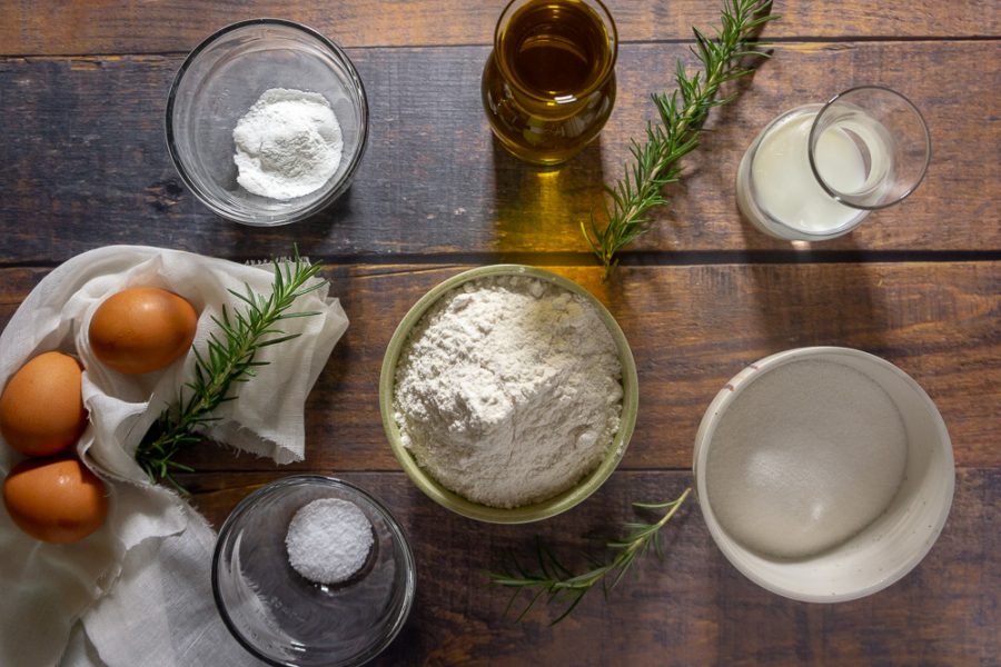 a collection of ingredients including flour, olive oil, eggs, sugar, rosemary and baking powder