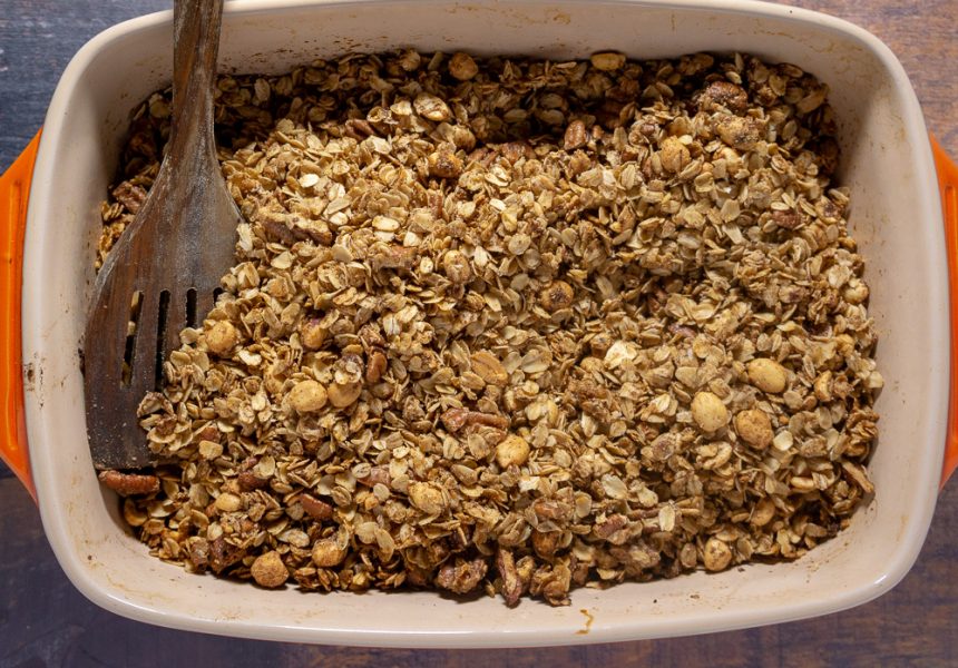 An orange casserole dish full of homemade granola with nuts.
