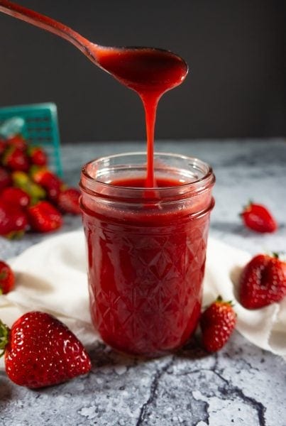 a jar of strawberry syrup with a spoon drizzling it