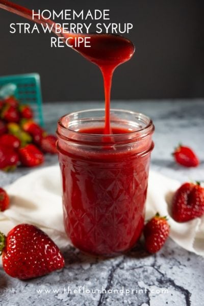 Strawberry syrup being drizzled from a spoon into a jar of syrup